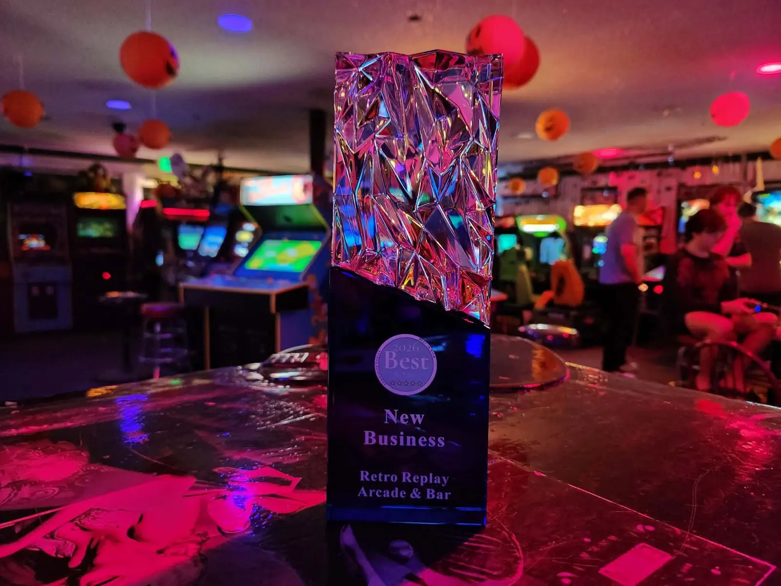 Crystal 2026 Best New Business award engraved Retro Replay Arcade & Bar, on the bar with the arcade behind it
